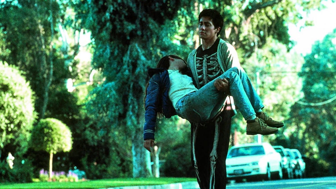 Donnie carrying Gretchen down a suburban street lined with trees