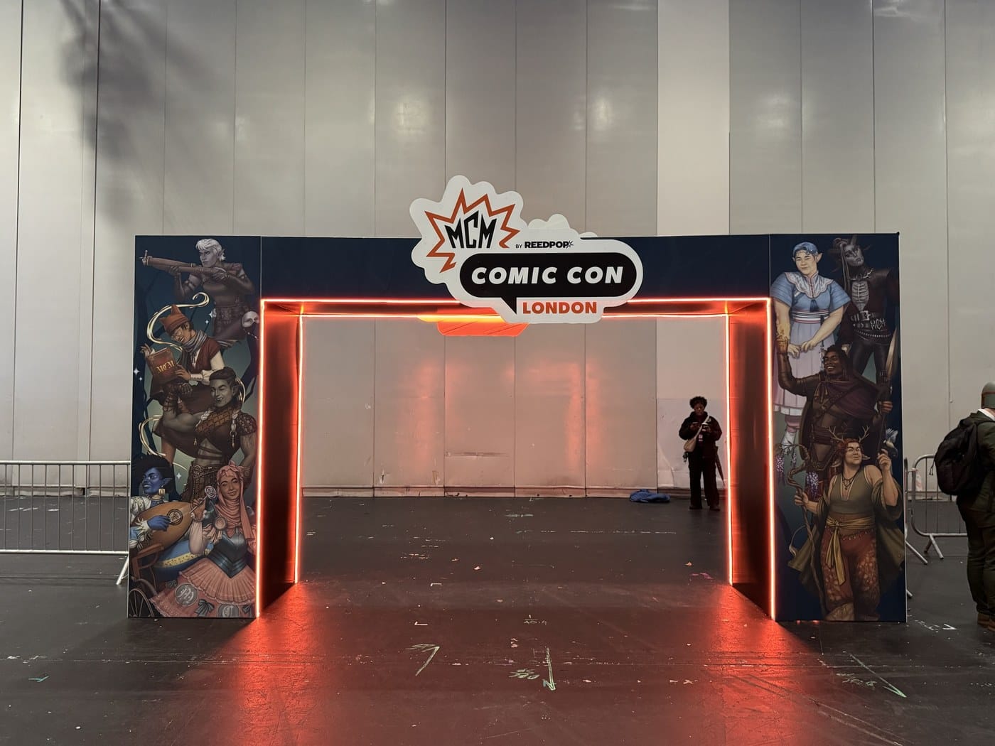 The MCM Comic Con London entrance arch at ExCeL, lit in orange neon and flanked by illustrations of a fantasy adventuring party