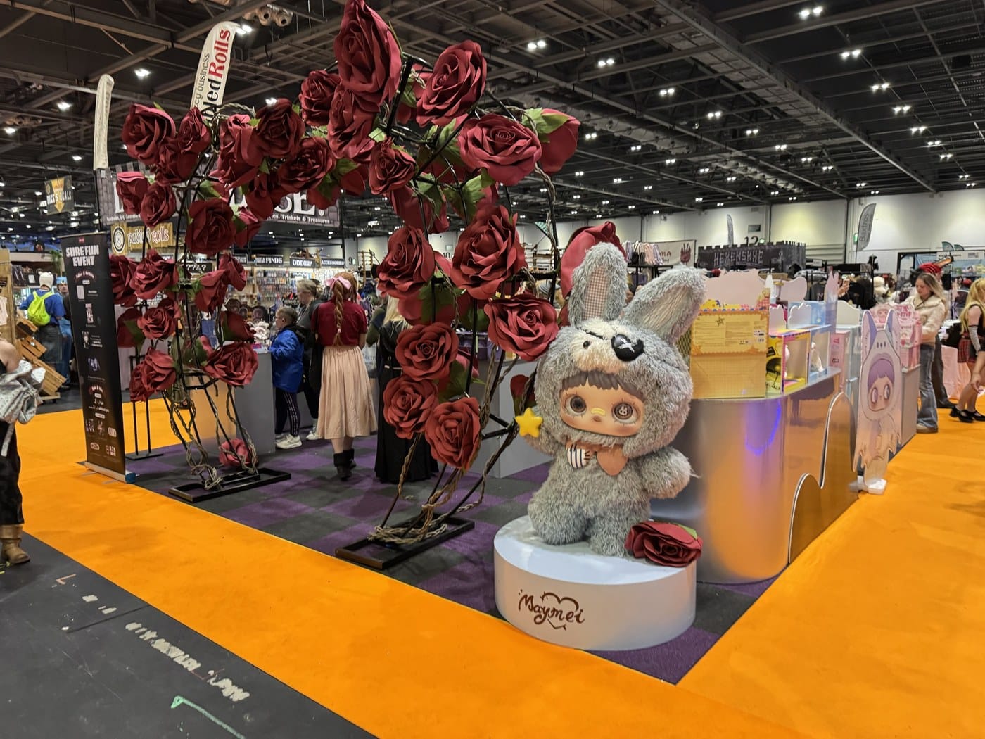The Maymei designer toy stand at MCM London, with an arch of giant red roses and a large Maymei figure in a grey bunny hood and eye patch