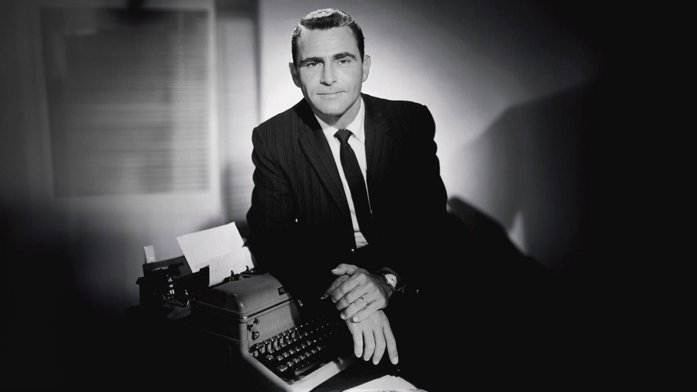 Rod Serling seated beside a typewriter in a dark studio